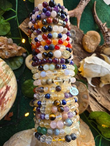 Bracelets de pierres précieuses multicolores empilés sur un support en bois.