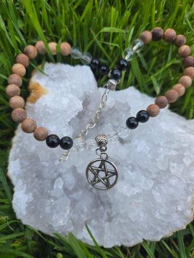 Bracelet en perles en bois et métal avec un pendentif pentacle, posé sur un cristal.